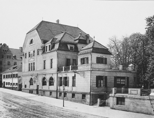 Der Neubau der »Betz'sche Gastwirtschaft« von der Törringstraße aus gesehen, um 1903. Links ist das Restgebäude der ehemaligen Grünwald-Gaststätte (dann Metzgerei) zu sehen, dahinter die Häuser der Ismaninger Straße. An der Vorderfront ist als Wandmalerei ein Münchner Kindl als schmuckes Wirtshausschild angebracht. (Evtl. von Franz Ringer?) Scan aus: Blätter für Architektur und Kunsthandwerk, Tafel 105, Berlin 1903.