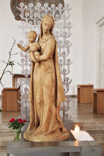 Die monochrome, unbehandelte und freistehende Holzfigur der Maria mit dem Jesuskind auf dem Arm wird als »Maria Immaculata« Prof. Theodor Georgii zugeschrieben. Aber im Nachlass des Künstlers gibt es keinen Hinweis zu dieser Arbeit. Da die Figur auch stilistisch nicht den Werken des Künstlers entspricht, scheint eine Verwechslung mit der »Immaculata im Schrein« (um 1934) vorzuliegen. hpt © Verein für Stadtteilkultur im Münchner Nordosten e.V., 2021
