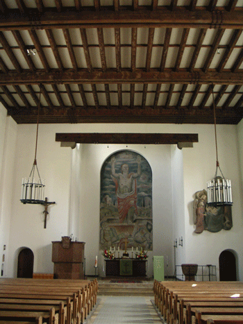 Altarraum Dreieinigkeitskirche, 2007. Das Altarbild »Auferstehung Jesu Christi« aus dem Jahr 1937 stammt von dem aus Bonn gebürtigen Maler Prof. Heinrich Brüne (1869–1945) und ist eines der wenigen erhaltenen Wandgemälde dieser Zeit. Links davon hängt ein Holzkruzifix aus der Augsburger Schule um 1700, rechts davon ist das 2 Meter große Holzrelief »Christi Geburt« der Bildhauerin Ruth Speidel (geb. 1916) aus dem Jahr 1948 zu sehen. Den Auftrag zu dieser Arbeit erhielt sie 1944, die erste Ausführung wurde jedoch bei einem Bombenangriff ein Raub der Flammen. Die jetzige Fassung aus Lindenholz entstand nach dem Krieg. Von der in Bogenhausen lebenden Künstlerin stammt auch das Relief »Der kniende Christus« (1938) am Taufstein aus Ruhpoldinger Marmor. hpt © Verein für Stadtteilkultur im Münchner Nordosten e.V.