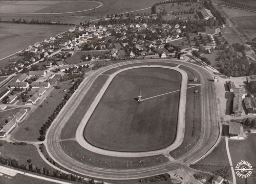 Luftbildaufnahme Trabrennbahn Daglfing um 1962. Im Hintergrund das Dorf Daglfing, am Ende der heutigen Burgauerstraße; die rein dörfliche Struktur der Daglfinger Gemeinde ist deutlich erkennbar, © Verein für Stadtteilkultur im Münchner Nordosten e.V.