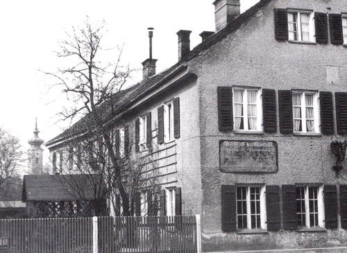 direkt neben dem "Bogenhauser Hof" stand eine Schlosserwerkstätte (vormals Bauernanwesen) an der Ismaninger Straße. Das Gebäude wurde 1969 abgebrochen, Stand 2014 steht hier ein fünfgeschossiges Wohnhaus. Im Hintergrund die Kirche St. Georg. (Foto aus dem Jahr 1938) © Verein für Stadtteilkultur im Münchner Nordosten e.V.