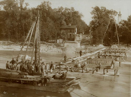 Bau einer Notbrücke durch die 3. Kompanie des Königlichen Eisenbahn-Bataillons im September 1899 nach der Isar-Hochwasserkatastrophe. Im Hintergrund der Turm von St. Georg. © Stadtarchiv München, Sign. DE-1992-FS-AB-STB-063-01