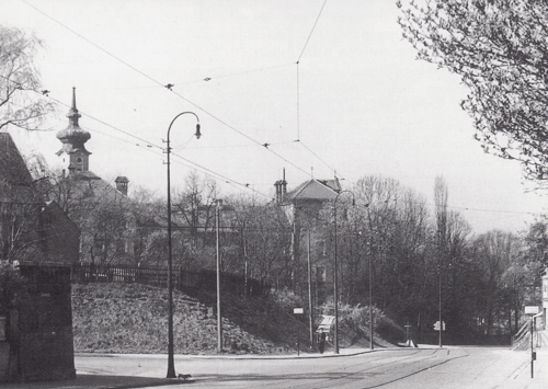 Blick auf die Montgelasstraße an der Ecke Törringstraße in Richtung stadteinwärts,1939. Im Vordergrund links eingezäunt Teile des ehemaligen Kaffl'schen Anwesens (Bogenhausen Hausnummer 14, später Lortzingstraße 1) neben dem sich einst die »Betz'sche Gastwirtschaft« befand, dann das Togalwerk, dahinter die alte Bogenhausener Schule und der Turm von St. Georg.