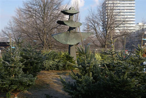 Die von Friederichsen als Brunnen konzipierte Skulptur inmitten des weihnachtlichen Christbaumverkaufs 2007. Bis 1964 befand sich genau an ihrem Standort eines der Zollhäuser der Stadt München. Es war dort seit 1893 in Betrieb. hpt © Verein für Stadtteilkultur im Münchner Nordosten e.V. , 2007.